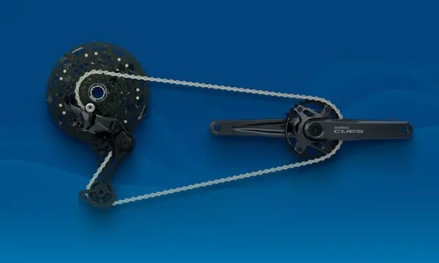 Zestaw napędowy **Shimano CUES**: przerzutka tylna, kaseta i korba z zębatkami, połączone łańcuchem na niebieskim tle.