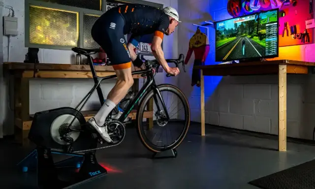 Intensywny trening na trenażerze kolarskim w wirtualnym świecie. Kolarz w stroju sportowym pedałuje, śledząc trasę na ekranie.