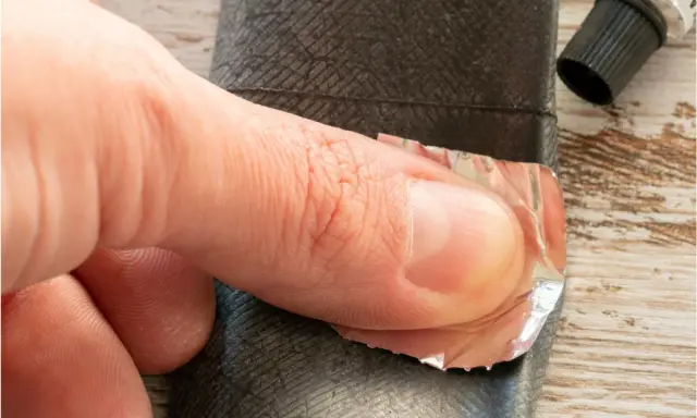 Dłoń przykleja łatkę do dętki roweru z przerzutką w piaście.