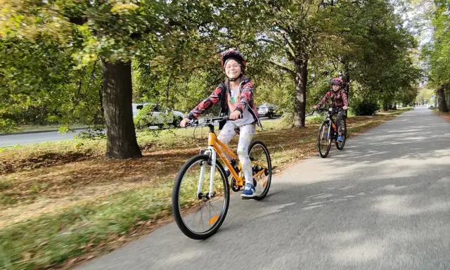 Dzieci na rowerach 24 cale na jaki wzrost? Uśmiechnięta dziewczynka na pomarańczowym rowerze i jej koleżanka cieszą się jazdą po alei.