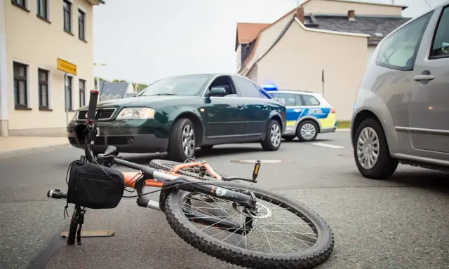 Wypadek drogowy: przewrócony rower, samochód i radiowóz policyjny. Maksymalne obciążenie roweru mogło przyczynić się do zdarzenia.