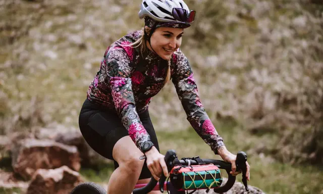 Uśmiechnięta rowerzystka w kwiecistej bluzie pokonuje kolejne kilometry. 100 km na rowerze to wyzwanie, ale radość z jazdy jest widoczna.