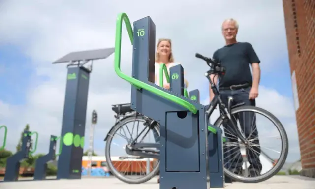 Stacja ładowania rowerów elektrycznych zasilana energią słoneczną. Para ludzi korzysta z nowoczesnych stojaków.