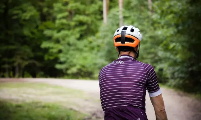 Kolarz w kasku i koszulce w paski jedzie ścieżką przez las. Idealny rower crossowy na takie wyprawy.