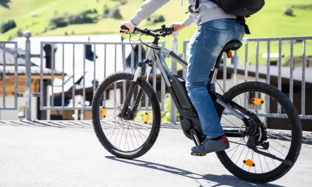 Osoba na rowerze elektrycznym, korzystająca z dofinansowania PFRON. W tle zielone wzgórza i zabudowania.
