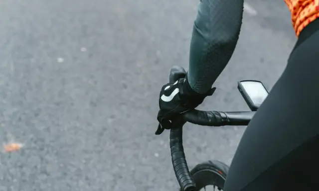 Rowerzysta w rękawiczkach z logo, trzymający kierownicę szosową. Kluczowe jest, jak dobrać szerokość kierownicy szosowej dla komfortu.