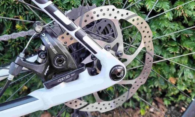 Regulacja hamulca tarczowego mechanicznego w rowerze. Widoczny zacisk TRP, tarcza hamulcowa i fragment ramy.