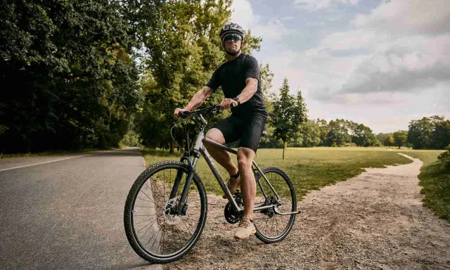 Mężczyzna w kasku i okularach jedzie na rowerze typu cross po leśnej ścieżce.
