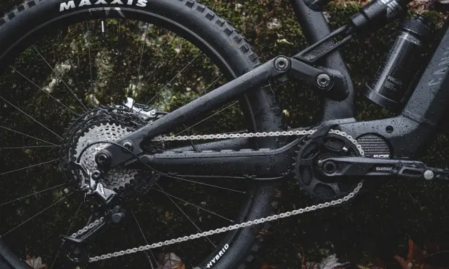 Część roweru elektrycznego z napędem **Shimano EP8** w deszczu. Widoczna kaseta, przerzutka, łańcuch i korba.