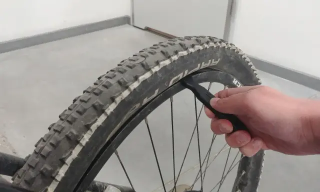 Dłoń używa łyżki do opon do wymiany opony w rowerze.