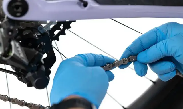 Ręce w niebieskich rękawiczkach sprawdzają stan łańcucha rowerowego. Dowiedz się, co ile wymieniać łańcuch w rowerze, by uniknąć awarii.
