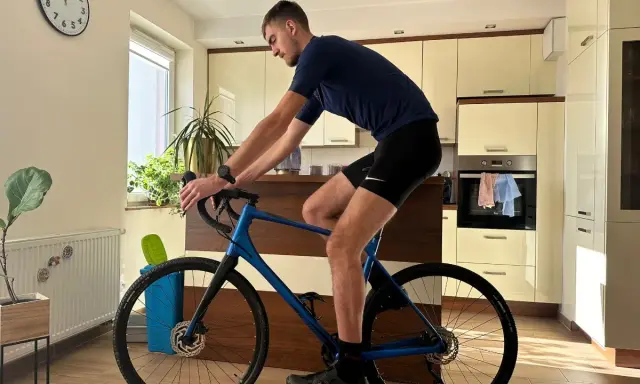 Mężczyzna w stroju kolarskim ćwiczy na rowerze gravel w domu. Poprawna pozycja na rowerze gravel jest kluczowa dla komfortu i wydajności.