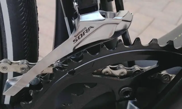 Montaż przedniej przerzutki Shimano Sora na rowerze. Widoczny fragment mechanizmu korbowego i łańcucha.