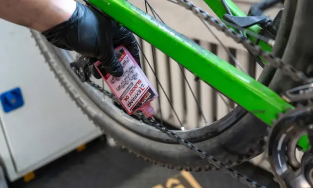Rękawiczka z czarną gumką aplikuje różowy olej do łańcucha roweru. To część przeglądu roweru, aby zapewnić płynną jazdę.