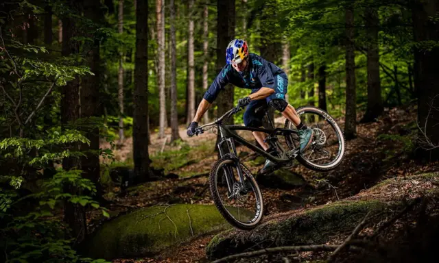 Kolarz w kasku Red Bull zjeżdża rowerem po leśnym stoku. To jest właśnie downhill – szybka jazda w dół!