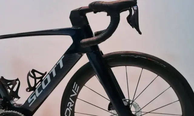 Ciemnoniebieski rower Scott z aerodynamicznym mostkiem i kierownicą. Koła z oponami Schwalbe Pro One.