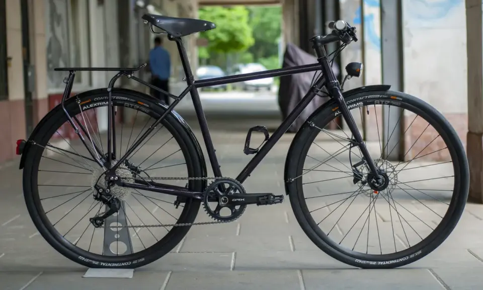 Ciemny rower gravel z błotnikami, bagażnikiem i oświetleniem, gotowy na każdą trasę.