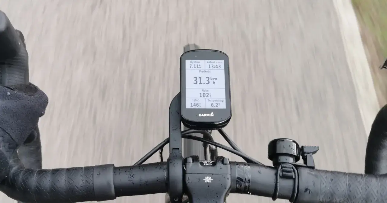 Na kierownicy roweru zamontowany jest licznik Garmin, który pokazuje dystans 7.11 km, tętno 146, rytm 102, temperaturę 6.2°C i aktualny czas 13:43. Prędkość 31.3 km/h jest widoczna na ekranie.
