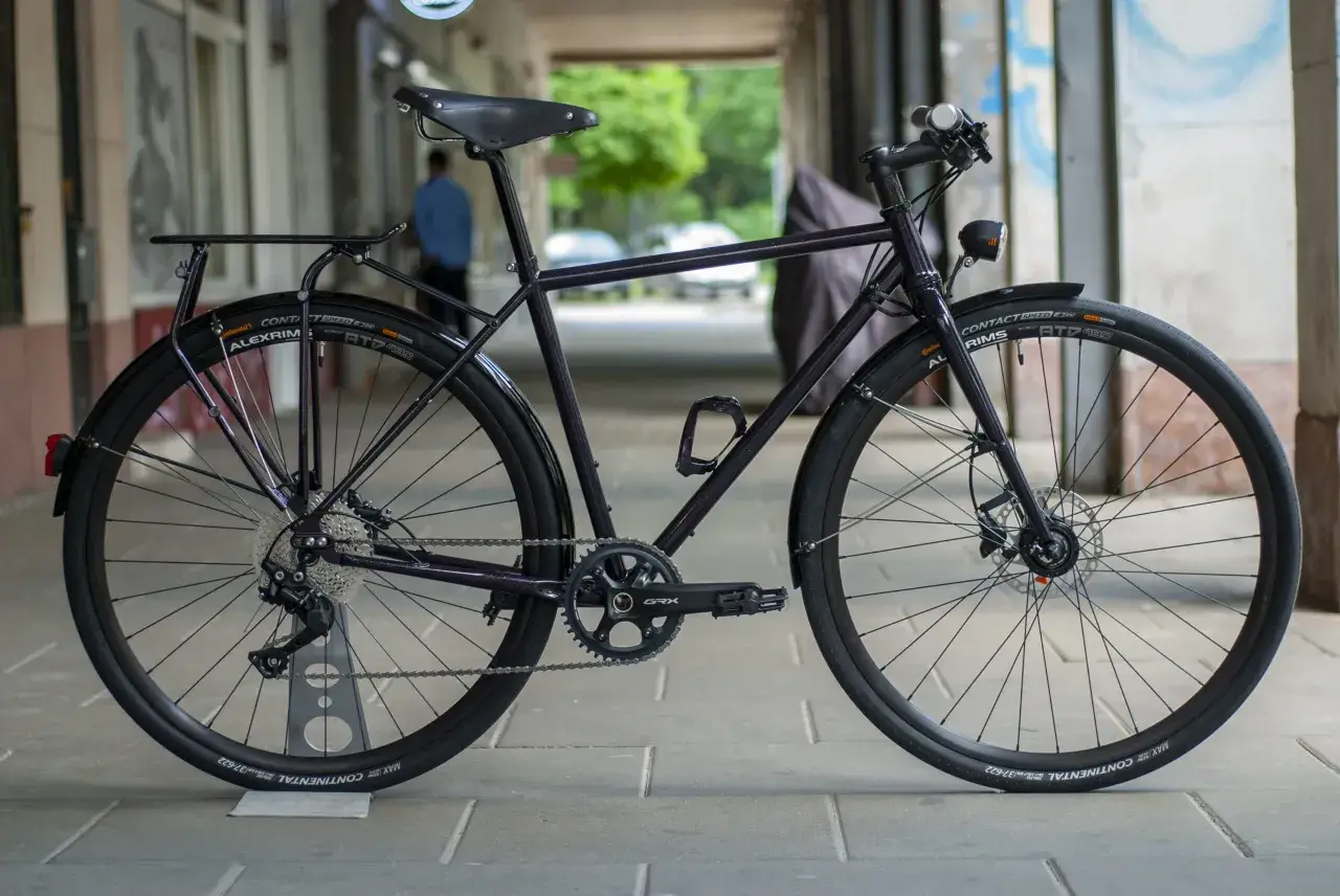 Ciemny rower gravel z błotnikami, bagażnikiem i oświetleniem, gotowy na każdą trasę.