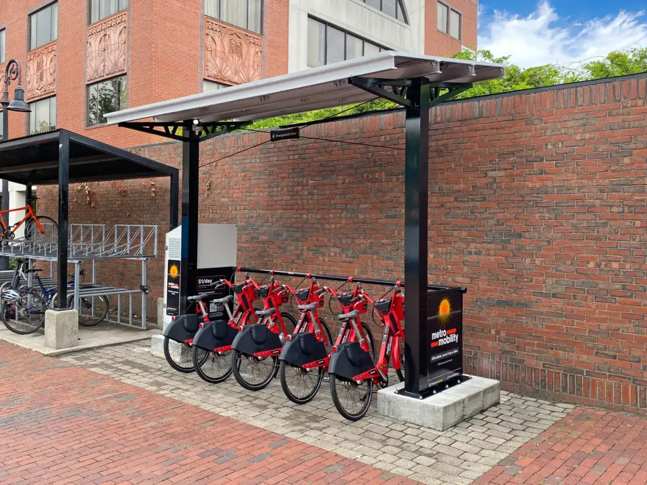 Stacja ładowania rower&oacute;w elektrycznych z czerwonymi rowerami gotowymi do jazdy. Panele słoneczne nadają jej ekologiczny charakter.