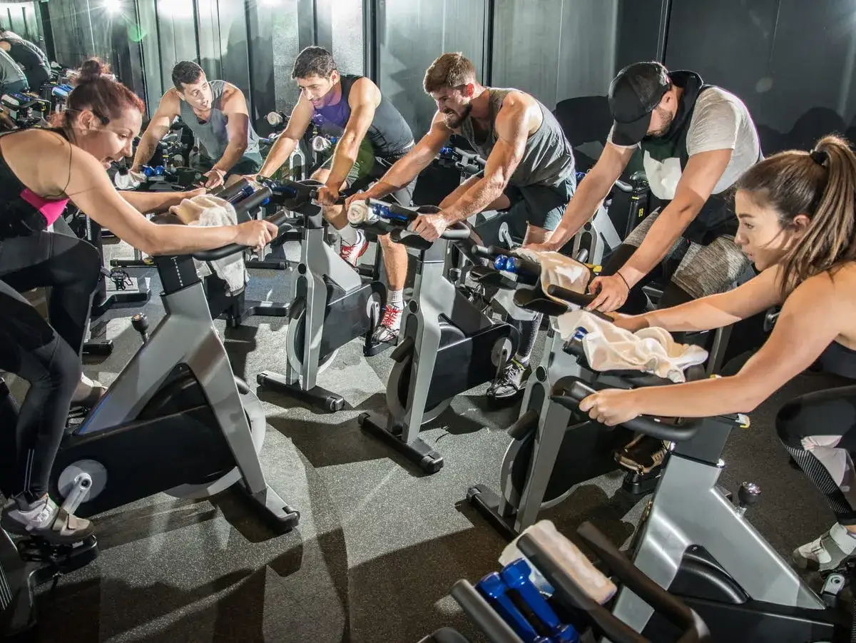 Grupa ludzi na zajęciach spinningowych. Intensywny trening na rowerach stacjonarnych, każdy skupiony na swoim wysiłku.