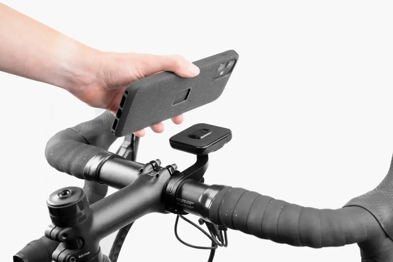 Dłoń zbliża telefon do czarnego uchwytu na kierownicy roweru. Idealny uchwyt na telefon do roweru, by mieć nawigację zawsze pod ręką.
