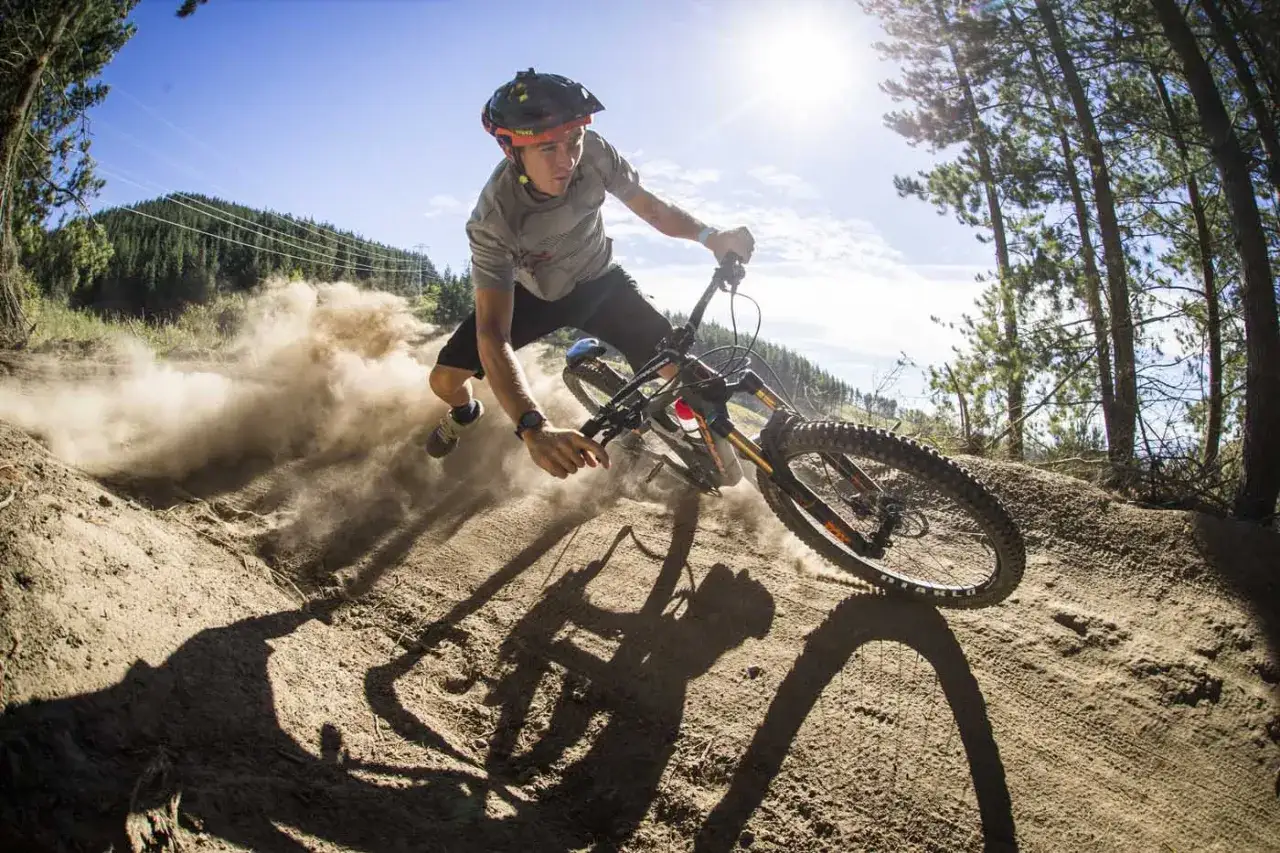 Kolarz MTB w dynamicznym zakręcie, unosząc kurz. Jego postawa to przykład prawidłowej pozycji na rowerze mtb, z ugiętymi kolanami i pochylonym tułowiem.