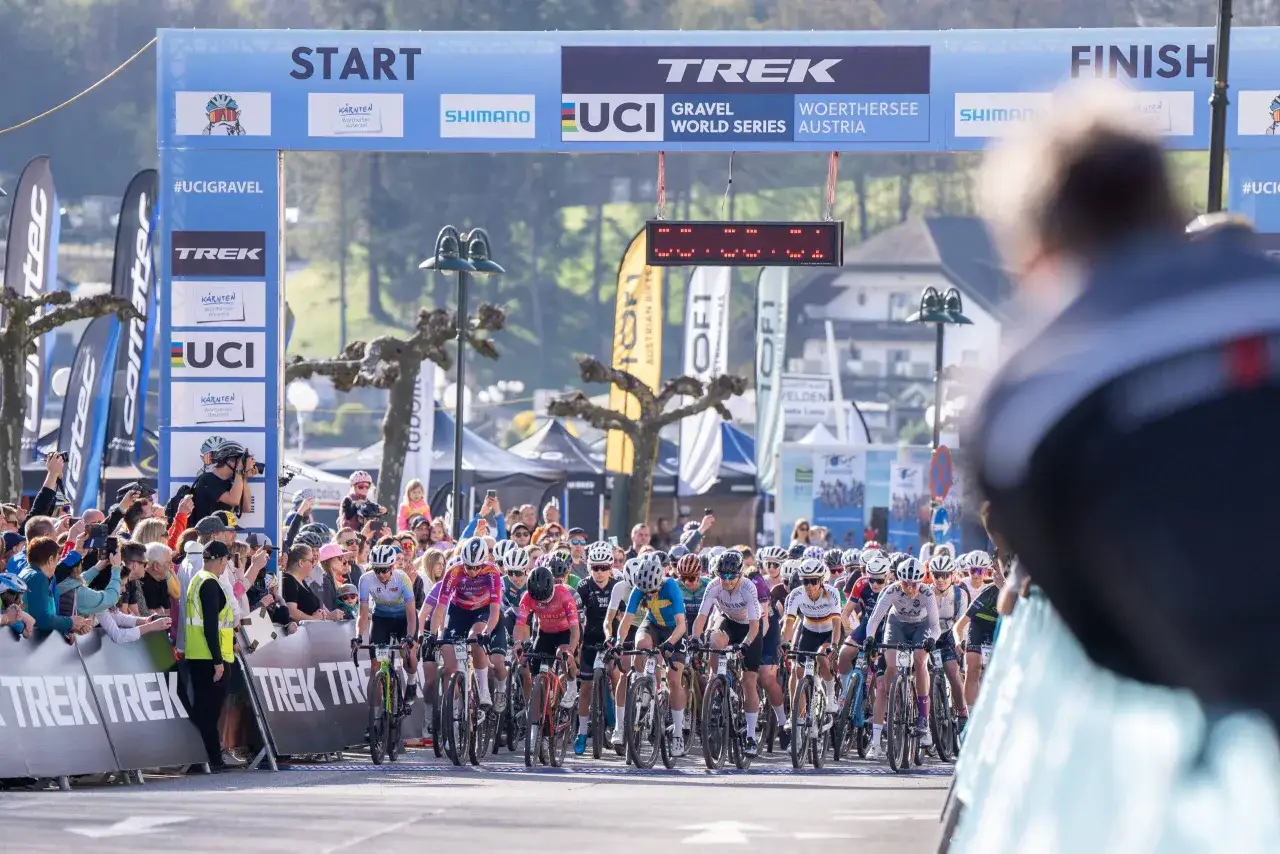 Kolarze gotowi do startu w wyścigu gravelowym UCI World Series w Austrii. Tłum kibic&oacute;w i banery sponsor&oacute;w.