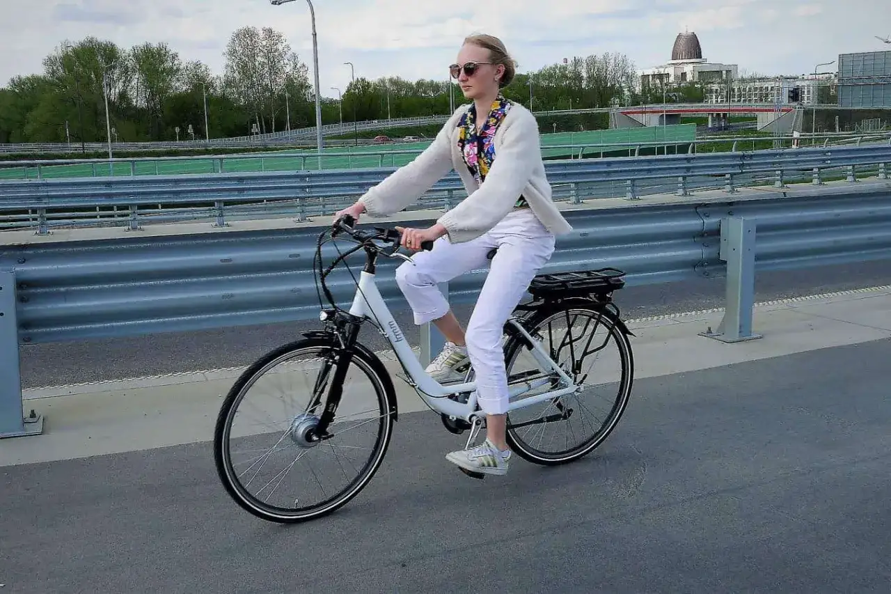 Kobieta na rowerze elektrycznym jedzie po moście. Uważaj, by nie dostać mandatu za rower elektryczny, jeśli nie spełnia on przepis&oacute;w.