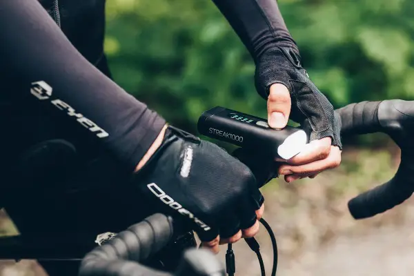Rowerzysta w rękawiczkach sprawdza mocne oświetlenie rowerowe STREAK1000. Dobre oświetlenie to podstawa bezpieczeństwa.