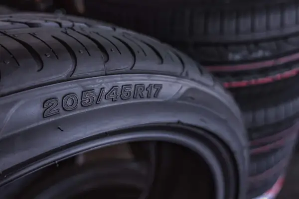 Zbliżenie na oponę z widocznymi oznaczeniami 205/45R17. W tle widać stos innych opon.