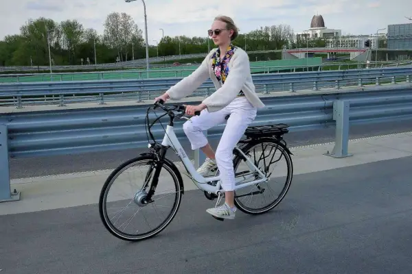 Kobieta na rowerze elektrycznym, ubrana na biało, jedzie po moście. Uważaj na przepisy, by nie dostać mandatu za rower elektryczny.