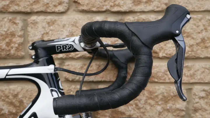 Czarna, wzorzysta owijka na kierownicę roweru szosowego z czarnymi manetkami Shimano.