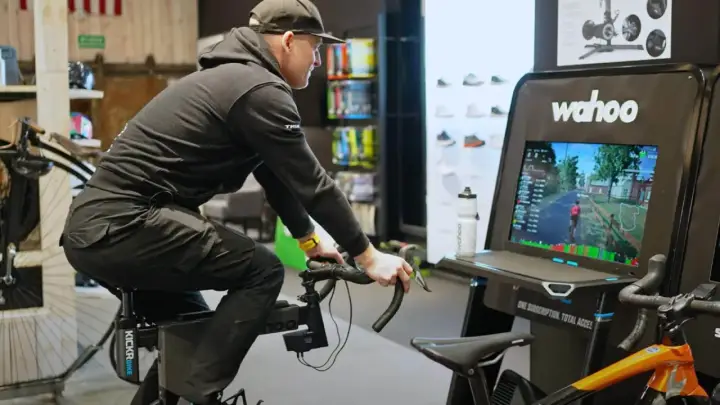Mężczyzna na rowerze stacjonarnym z napędem **direct drive** wirtualnie przemierza trasę, widoczną na ekranie Wahoo.