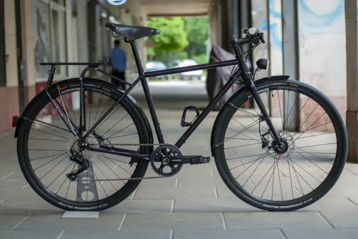 Ciemny rower gravel z błotnikami, bagażnikiem i oświetleniem, gotowy na każdą trasę.
