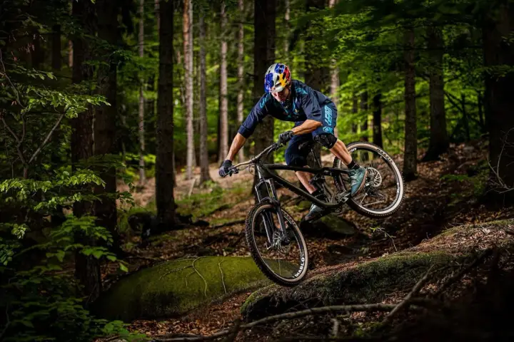 Kolarz w kasku Red Bull zjeżdża rowerem po leśnym stoku. To jest właśnie downhill – szybka jazda w dół!
