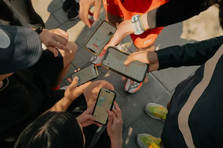 Grupa biegaczy analizuje swoje wyniki na telefonach. Widoczne ekrany aplikacji Strava po polsku pokazują mapy tras i statystyki.